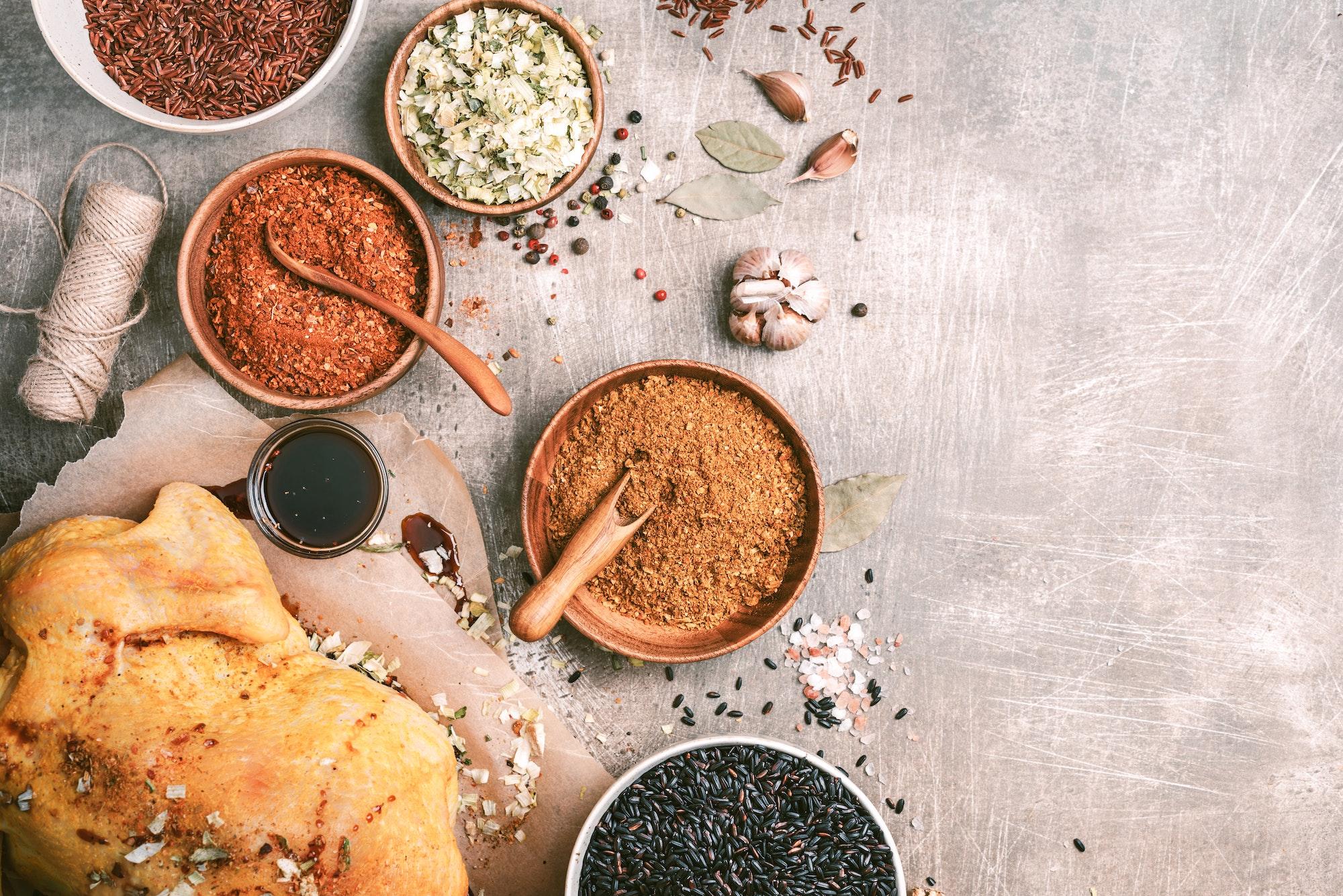 Cooking preparation of raw chicken with ingredients, spices, herbs, sauce and cooking spoon on grey