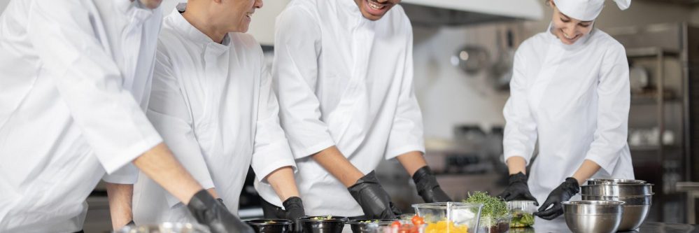 Multiracial team of cooks mixing ingredients for take away food in professional kitchen